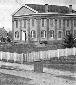 Monroe County’s second courthouse, completed in 1853, still stands today as the center section of the older half of the courthouse. The box-like device at the street’s edge was part of the public scale where wagons of farm products and other items could be weighed for sale.