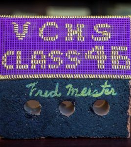Pictured is a brick from the old Valmeyer High School, complete with a purple cover embroidered by Fred Meister himself with his class.