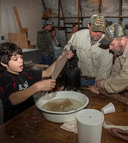 From left, Dallas Wessel, 11, of Milstadt, soaks each large sausage casing and hands it to Darren Reifschneider and Paul Vogt, both of Waterloo, to fill with a hand-cranked sausage stuffing machine.