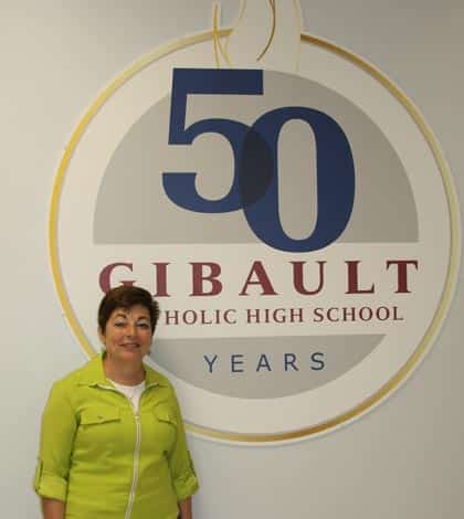 Sev Kovarik stands next to the school’s 50th anniversary sign at the main entrance. (Sean McGowan photo)