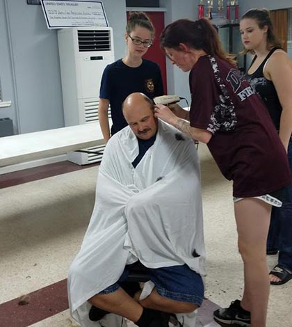 Dupo firefighter Paul Morris, who is battling stage 4 colon cancer, allows firefighter April Odehnal to shave his head at the fire station as his daughters Ashley (left) and Kaitlyn look on. (submitted photo)
