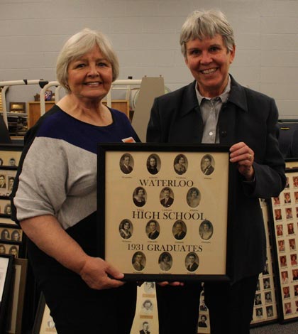 Pictured, from left, Janice Sanders Callahan and Mary Ellen Huetsch proudly display a restored photo of the Waterloo High School class of 1931. Behind them are the dozens of other restored photos that will be hung along the WHS Legacy Hall in the school. (Sean McGowan photo)